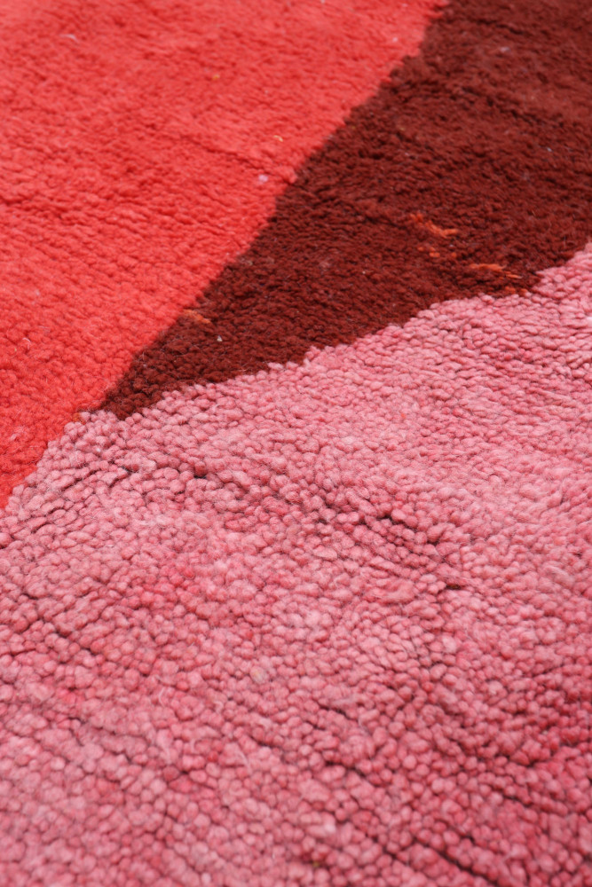 Tapis berbère aux couleurs vives, avec des motifs géométriques en rose, rouge et marron sur une texture douce.