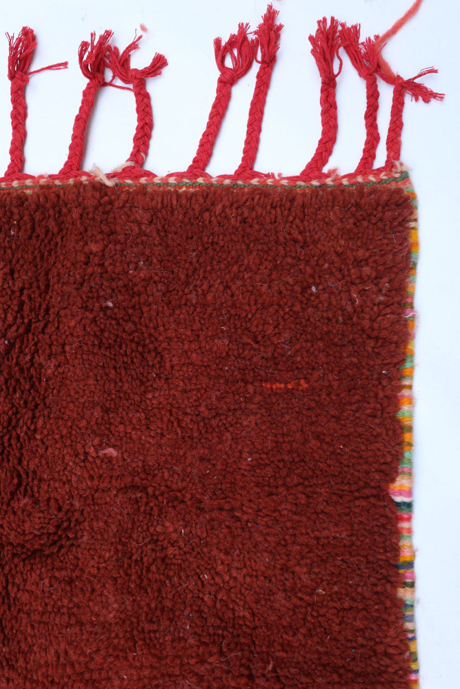 Tapis berbère en laine rouge profond avec motifs colorés et pompons, ajoutant une touche artisanale chaleureuse.