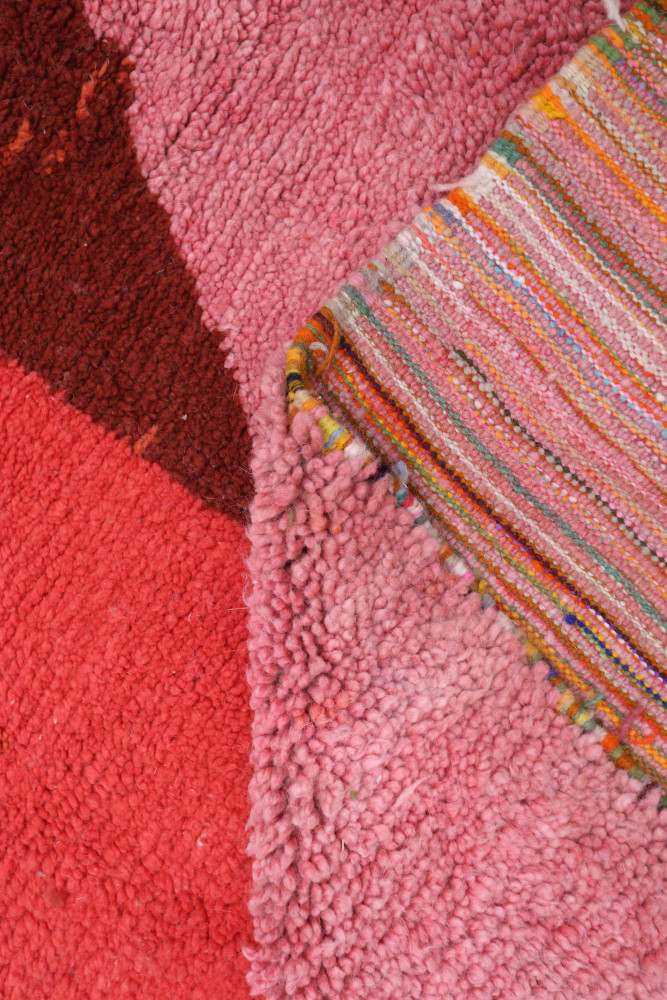 Tapis berbère aux teintes roses et rouges avec des motifs géométriques et une texture moelleuse, parfait pour un intérieur chale