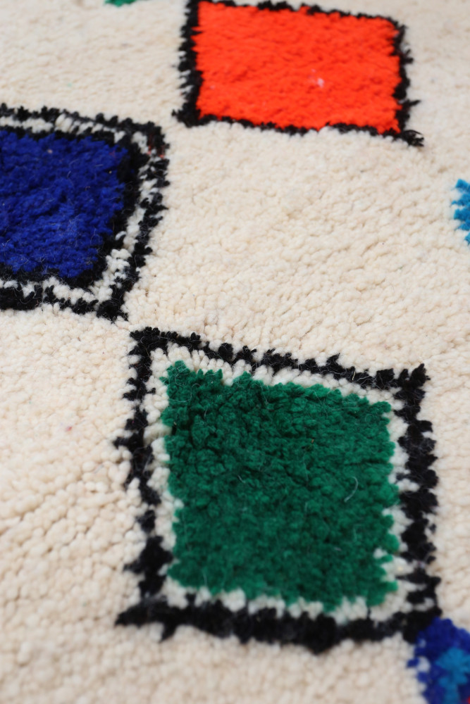 Tapis berbère avec un fond crème orné de carrés colorés en vert, bleu, rouge et noir, au design moderne et texturé.