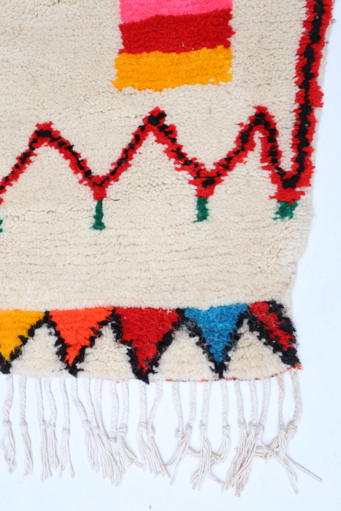 Tapis berbère aux motifs géométriques, couleurs vives comme le rouge, le jaune et le bleu sur fond crème.