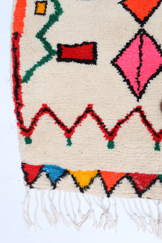 Tapis berbère aux motifs colorés avec des losanges roses, rouges et verts sur fond crème avec des bordures noires.