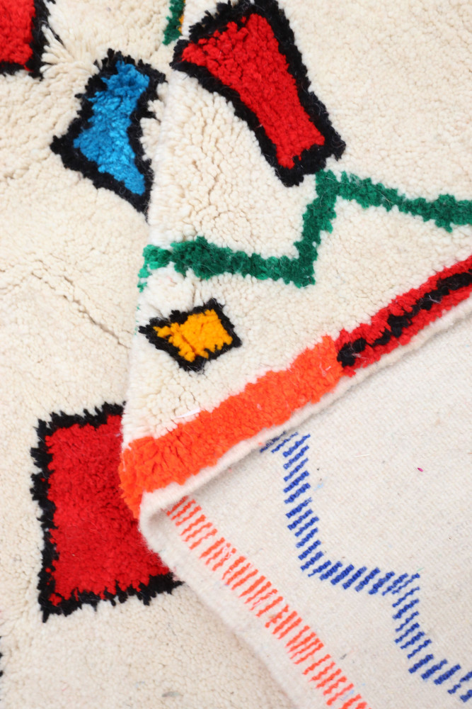 Tapis berbère aux motifs colorés avec des formes géométriques en rouge, bleu, vert et orange sur fond crème.