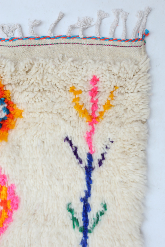 Tapis berbère aux motifs floraux multicolores avec des touches vives de rose, orange, bleu et jaune sur fond crème.
