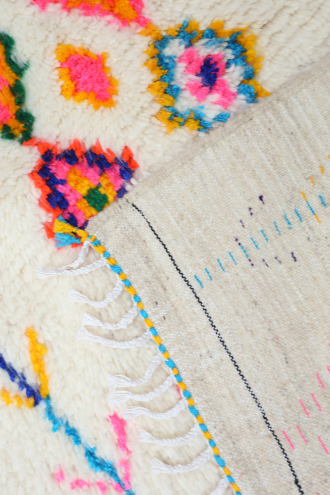 Tapis berbère aux motifs géométriques colorés, dominé par des teintes vives et un fond crème.