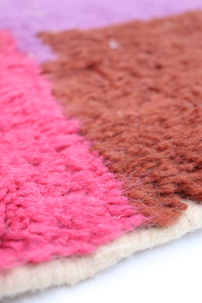 Tapis berbère aux motifs géométriques avec des tons de rose vif, violet et brun, apportant une touche moderne et chaleureuse.