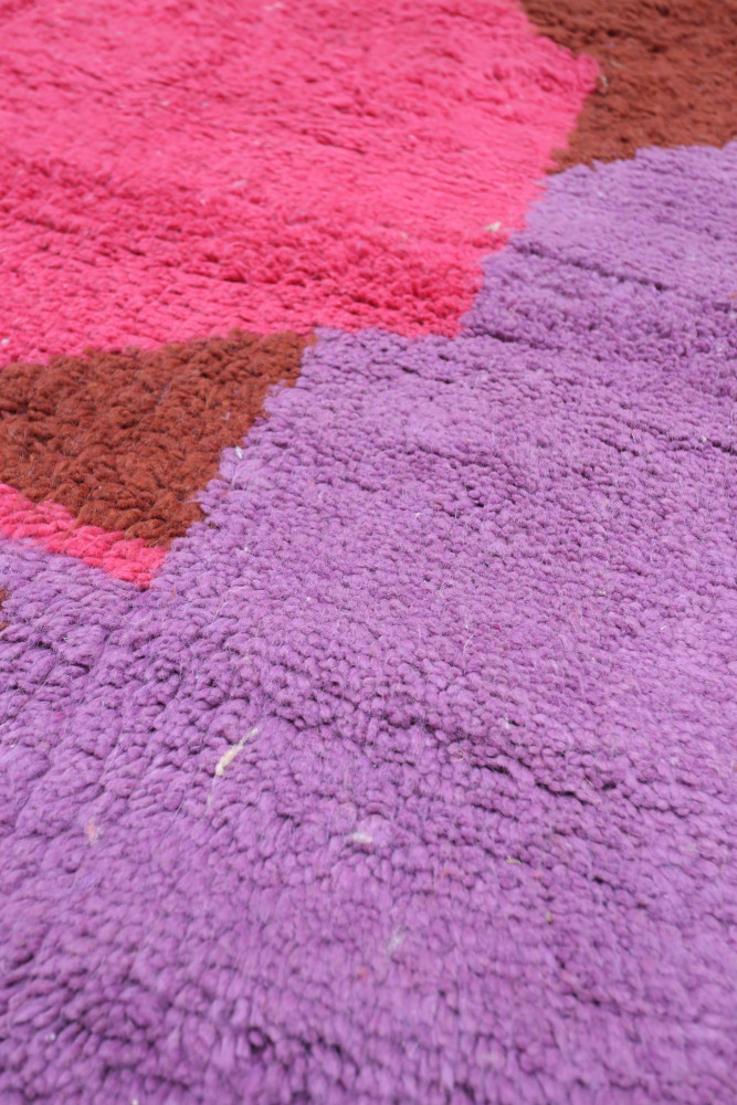 Tapis berbère aux motifs géométriques, dominé par des couleurs vives comme le rose, le violet et le marron.