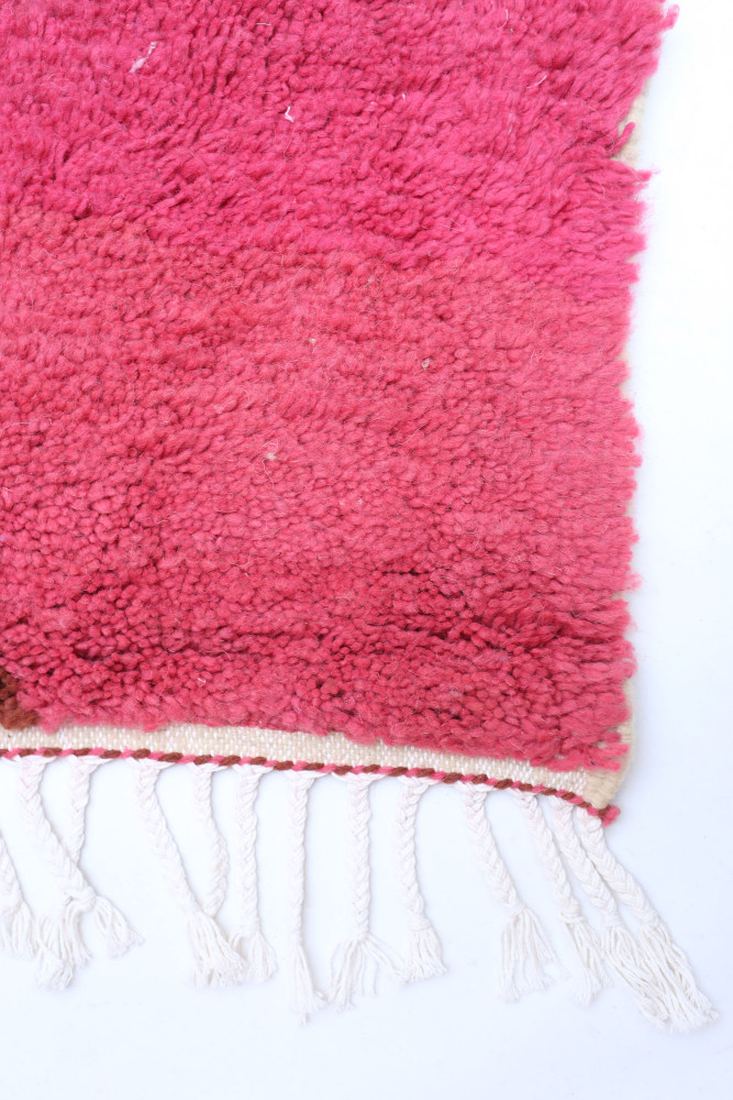Tapis berbère coloré en dégradé de rose avec motifs géométriques et franges blanches.