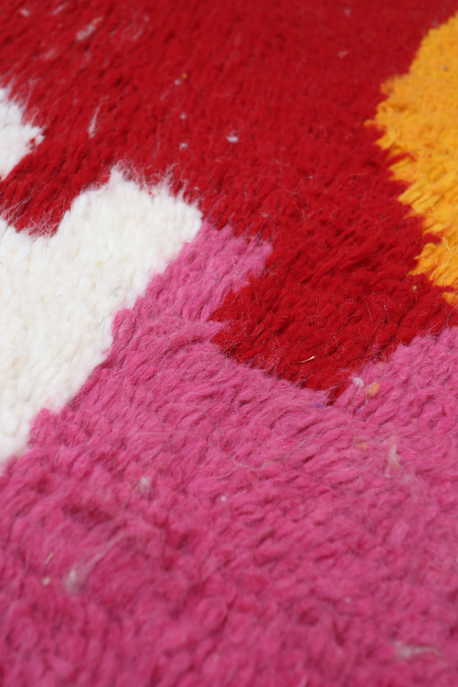 Tapis berbère aux motifs géométriques colorés, dominé par le rouge, le rose, le jaune et le blanc.