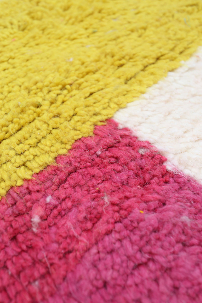 Tapis berbère coloré avec des motifs géométriques en jaune, rose et blanc, ajoutant une touche moderne à la décoration intérieur