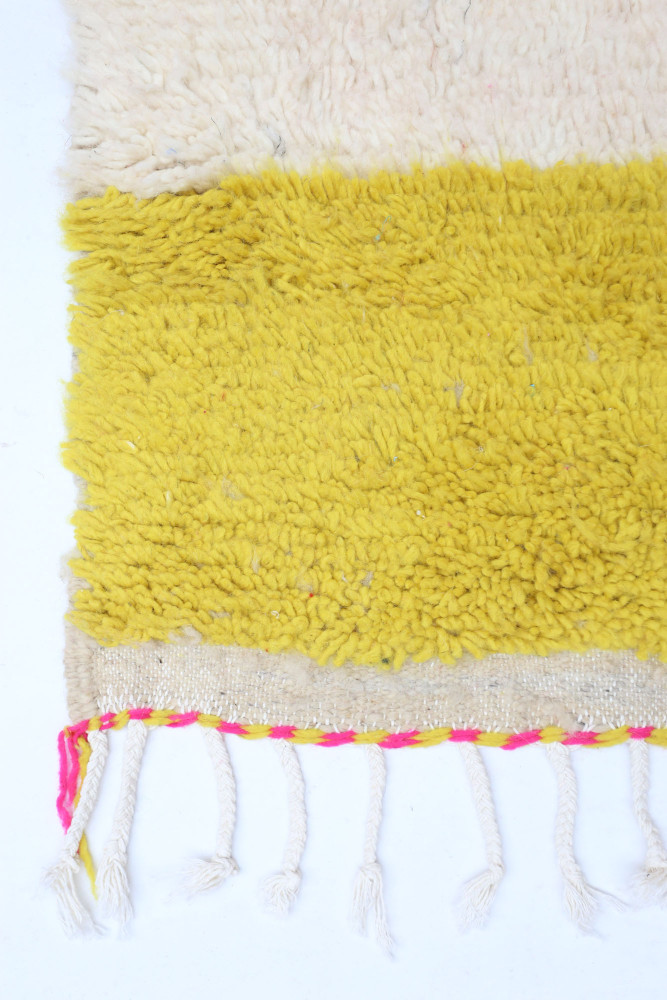 Tapis berbère au style moderne, avec des couleurs crème et jaune vif, ornés de motifs tissés et de franges colorées.