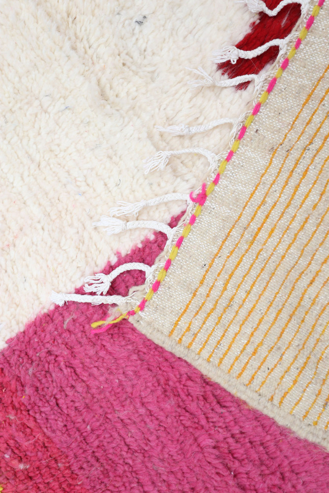 Tapis berbère coloré avec des motifs géométriques, dominé par des teintes blanches, fuchsia et des lignes jaunes.