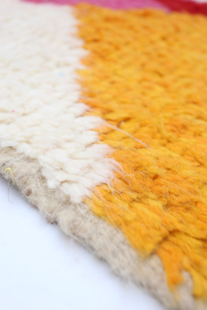 Tapis berbère aux teintes vives de jaune, blanc et beige, avec un style tissé à la main aux motifs géométriques.