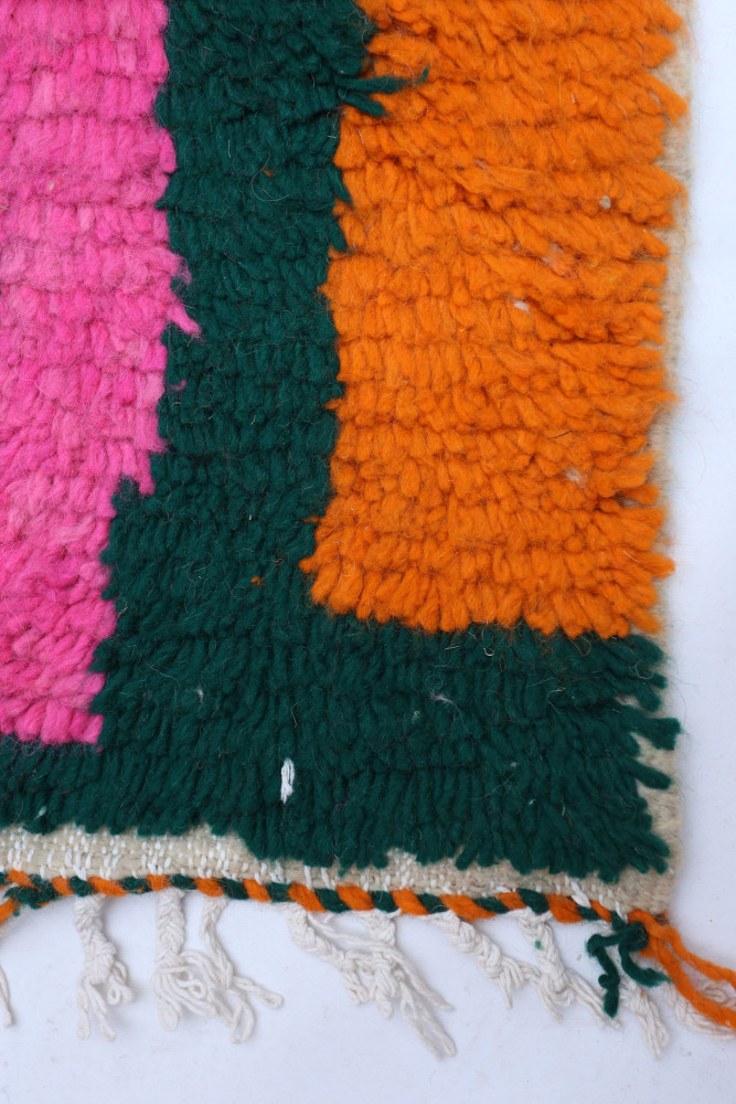 Tapis berbère coloré avec des motifs géométriques en rose, vert et orange, ajoutant une touche chaleureuse et dynamique.