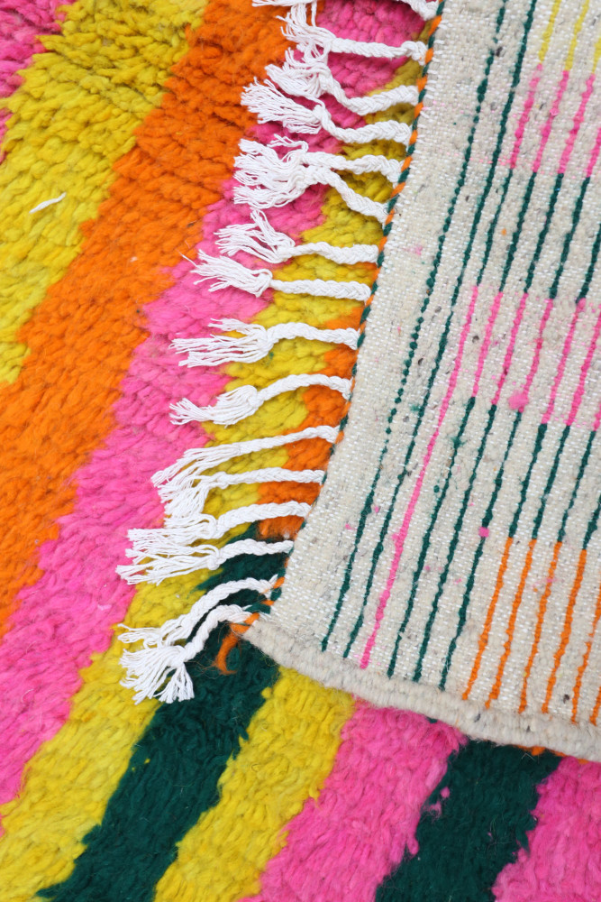Tapis berbère coloré avec des motifs géométriques, predominance de rose, jaune et vert.