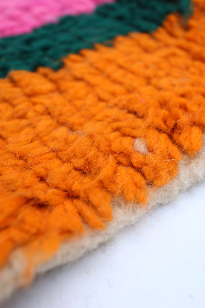 Tapis berbère coloré avec des motifs géométriques en orange, vert, rose et blanc, ajoutant une touche artisanale à votre intérie