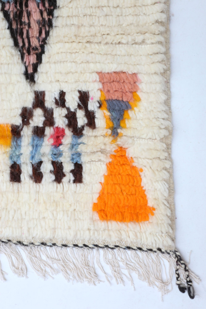 Tapis berbère aux motifs géométriques colorés dans les teintes crème, orange, rose et bleu, parfait pour un intérieur moderne.