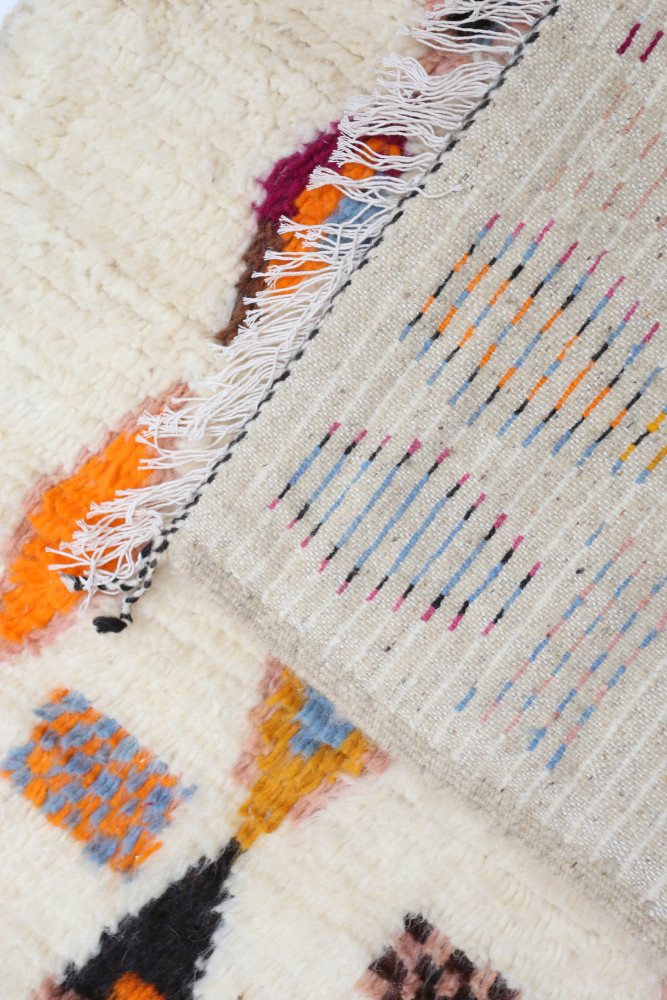 Tapis berbère contemporain aux motifs géométriques colorés, dominé par des teintes crème, orange et bleu.