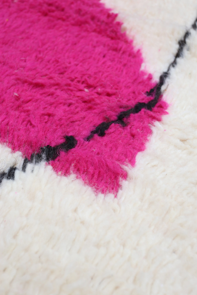 Tapis berbère coloré avec des motifs en rose vif et noir sur fond crème, ajoutant une touche moderne à votre décoration.