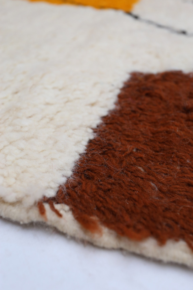 Tapis berbère en laine, aux teintes beige, marron et jaune avec motifs géométriques contemporains.