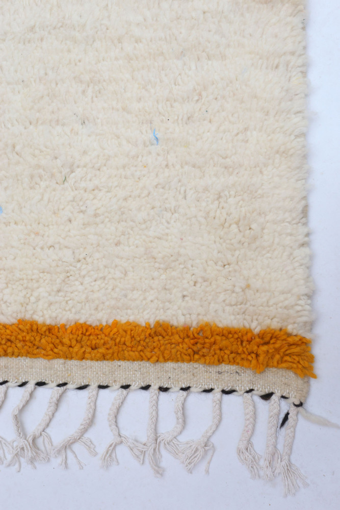 Tapis berbère en laine crème avec des motifs géométriques et une bordure orange, ajoutant une touche chaleureuse et authentique.