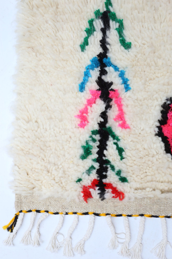 Tapis berbère aux motifs colorés en rose, bleu, vert et noir sur fond crème, parfait pour apporter une touche design.