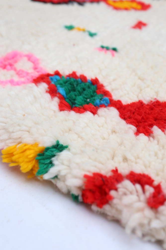 Tapis berbère aux couleurs vives et motifs floraux sur fond crème, ajoutant une touche chaleureuse à votre intérieur.