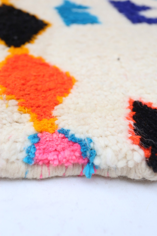 Tapis berbère aux motifs géométriques colorés avec des teintes vives comme le bleu, orange et rose sur fond crème.