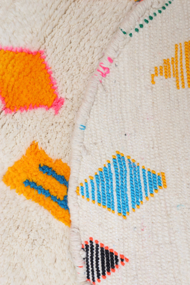 Tapis berbère aux motifs géométriques colorés avec des tons de blanc, orange, bleu et noir.