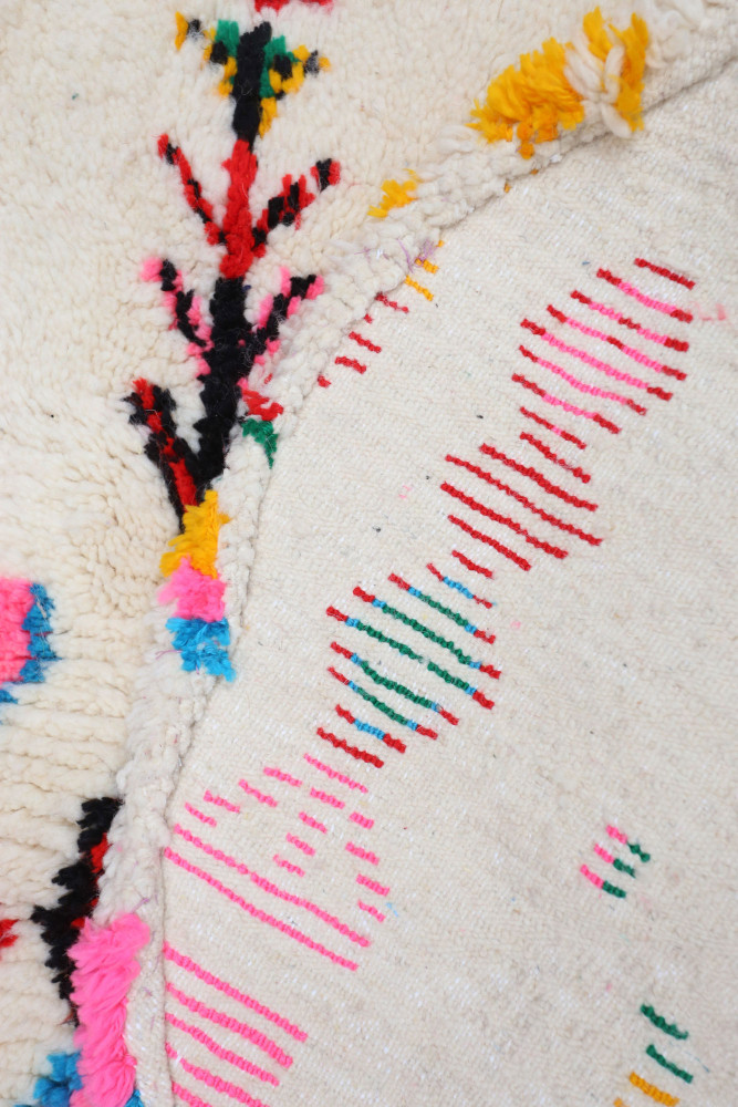 Tapis berbère coloré avec des motifs géométriques et floraux en rose, jaune, bleu et vert sur fond crème.