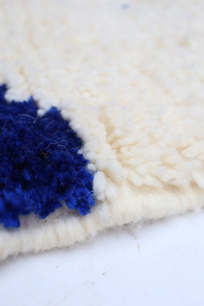 Tapis berbère en laine crème avec motifs bleus contrastés, alliant tradition et modernité.