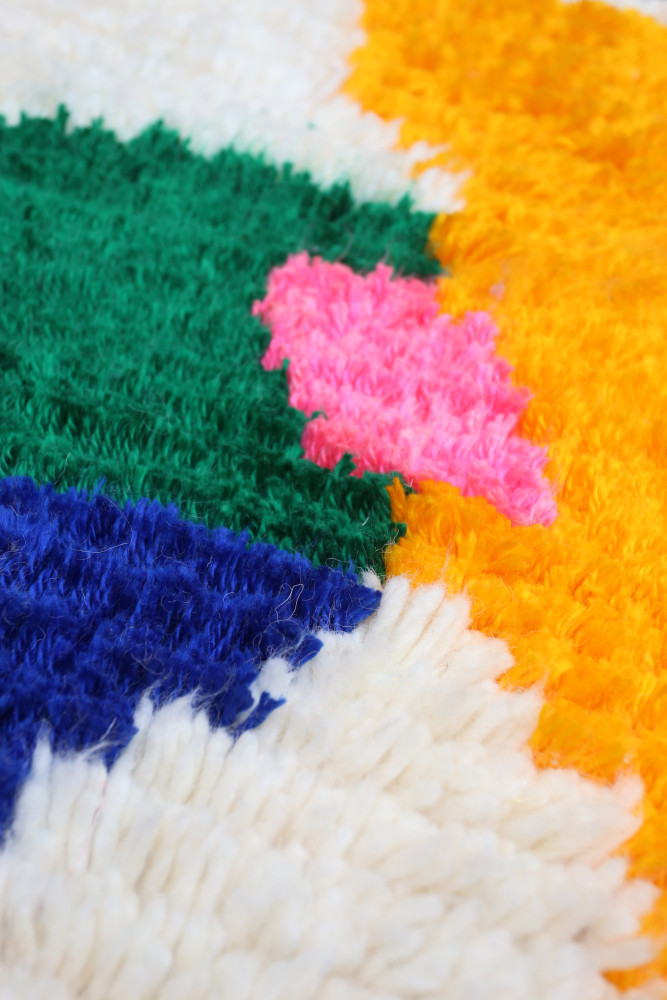 Tapis berbère coloré avec des motifs géométriques en vert, rose, jaune et bleu sur fond blanc.