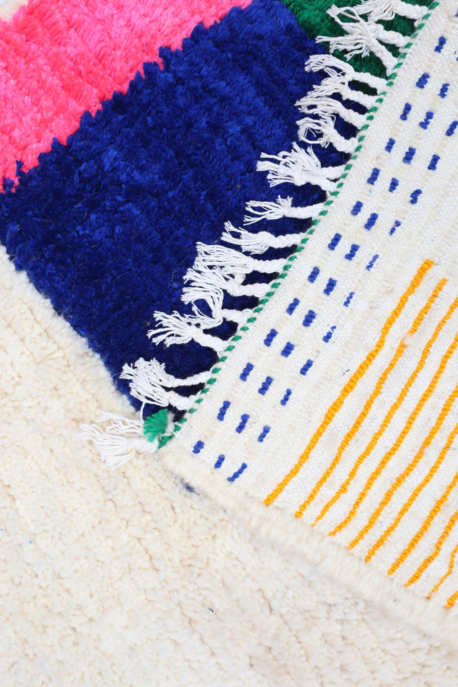 Tapis berbère coloré aux motifs géométriques, avec des nuances de rose, bleu, vert et blanc.