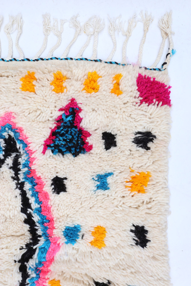 Tapis berbère avec des motifs colorés, dominé par des teintes crème, bleu, rose, orange et noir.