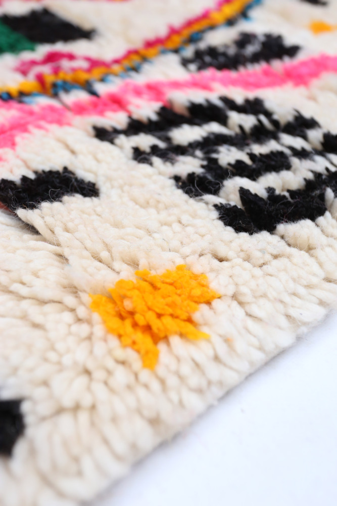 Tapis berbère aux motifs géométriques colorés, dominé par des teintes crème, noir, rose et jaune éclatant.