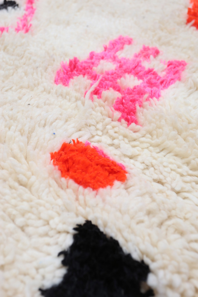 Tapis berbère au style géométrique, aux couleurs vives de rose, orange et noir sur fond crème.
