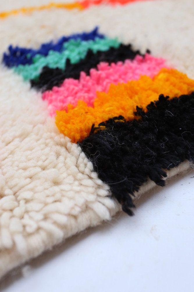 Tapis berbère en laine avec des motifs colorés en rose, orange, vert et noir sur fond crème, ajoutant une touche moderne.