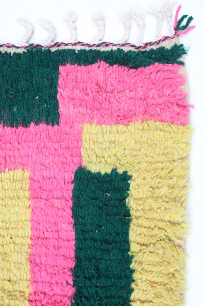 Tapis berbère aux motifs géométriques colorés avec des teintes de rose, vert et jaune.