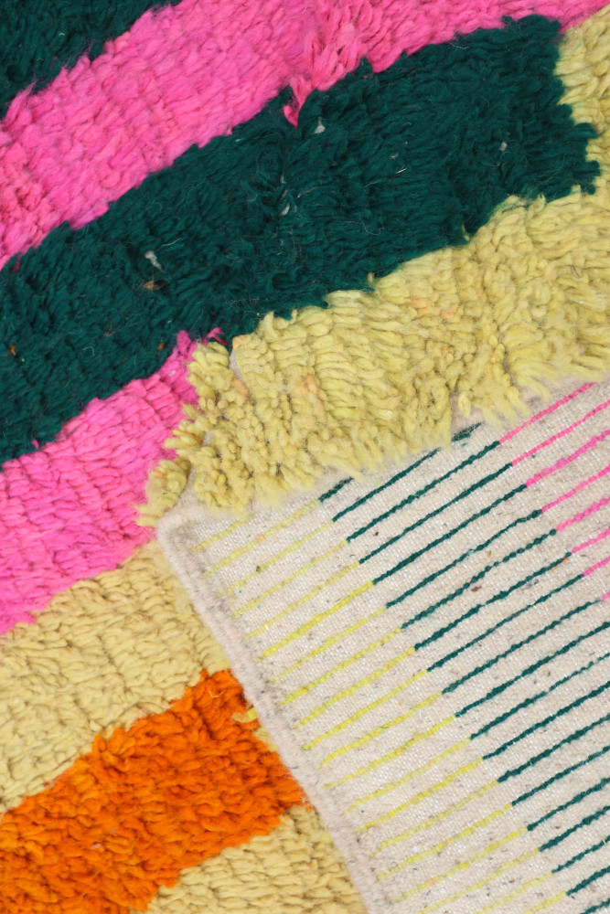 Tapis berbère coloré avec des motifs géométriques et des teintes vives de rose, vert, jaune et orange.