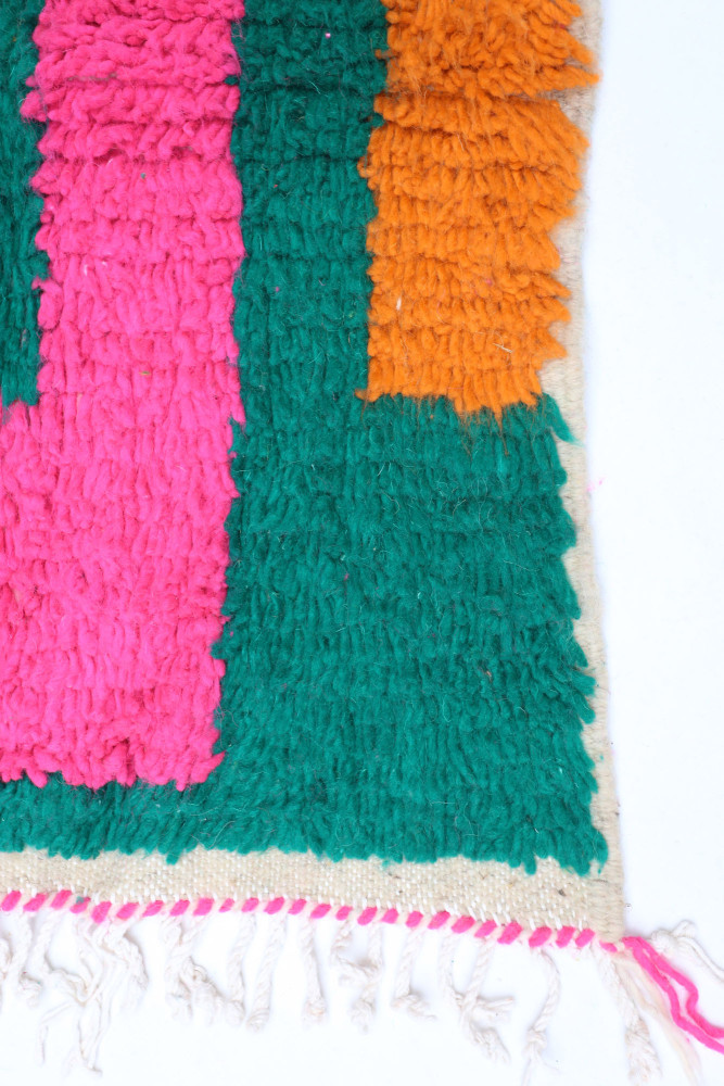 Tapis berbère coloré avec des motifs géométriques en vert, rose et orange, offrant une touche moderne et vibrante.