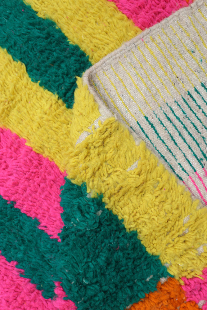 Tapis berbère coloré avec des motifs géométriques en rose, vert et jaune, apportant une touche vivante à votre intérieur.