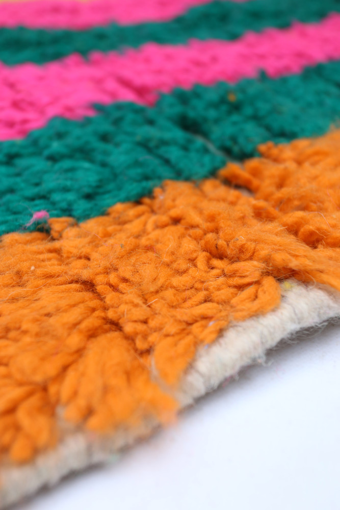 Tapis berbère coloré aux motifs géométriques avec des rayures roses, vertes et orange.