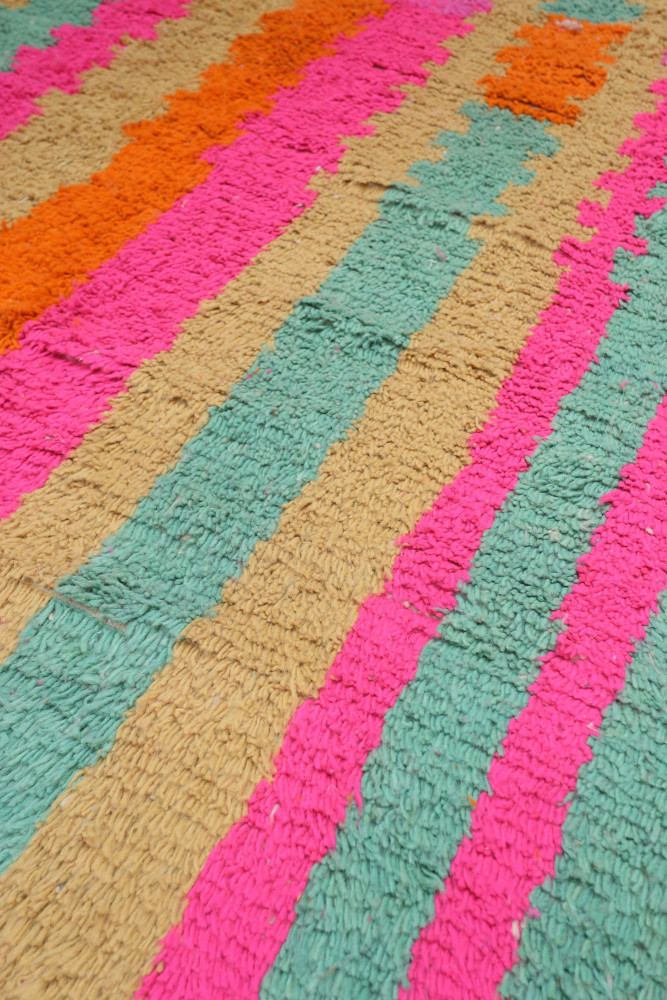 Tapis berbère coloré avec des motifs géométriques en rose, orange, vert et beige, ajoutant une touche contemporaine.
