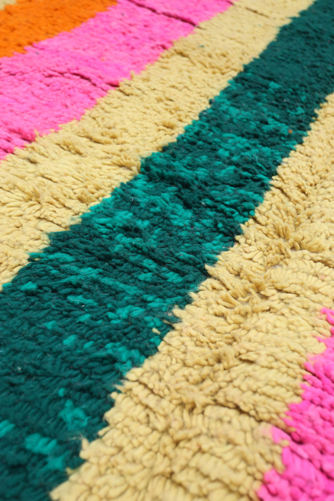 Tapis berbère coloré avec des motifs vibrants en rose, orange et vert sur une texture douce et pelucheuse.