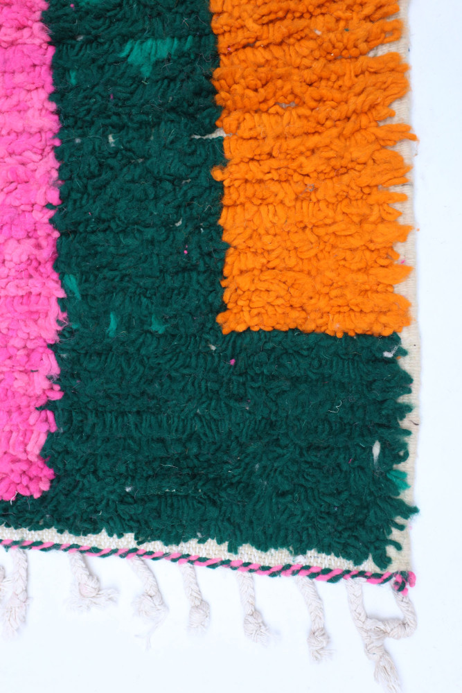 Tapis berbère coloré en vert, rose et orange avec des motifs texturés et des franges traditionnelles.