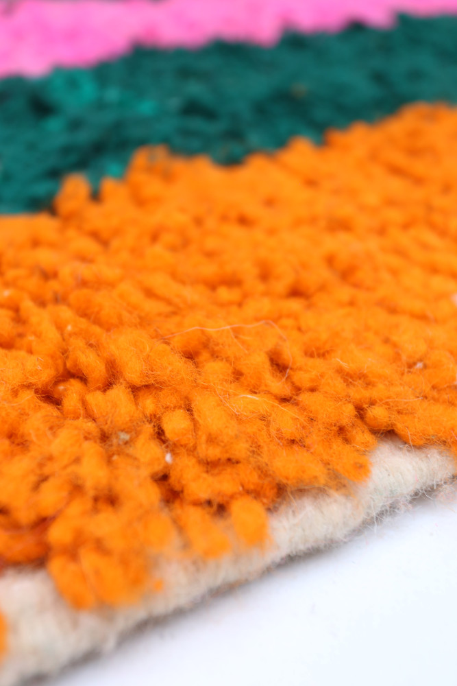 Tapis berbère coloré avec des nuances vives d\'orange, vert et rose, présentant des motifs texturés et modernes.