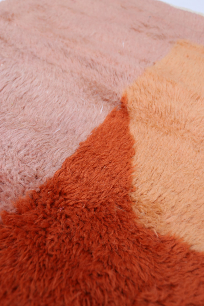 Tapis berbère moderne aux couleurs pastel, avec des motifs géométriques en nuances de rose et orange.
