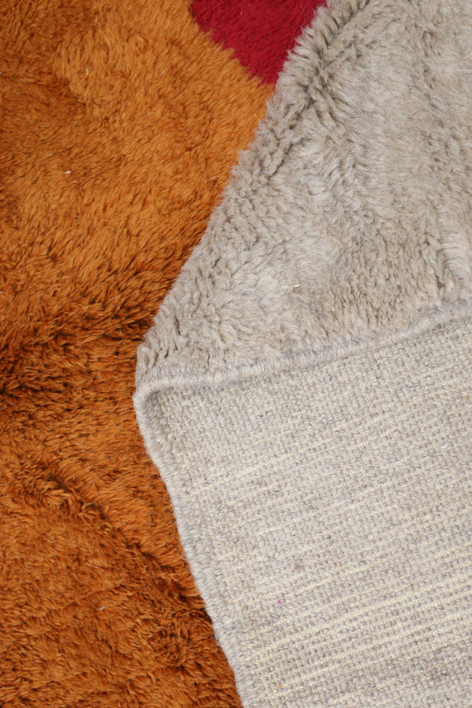 Tapis berbère en laine, aux tons de brun, camel et rouge, avec un motif texturé et chaleureux.