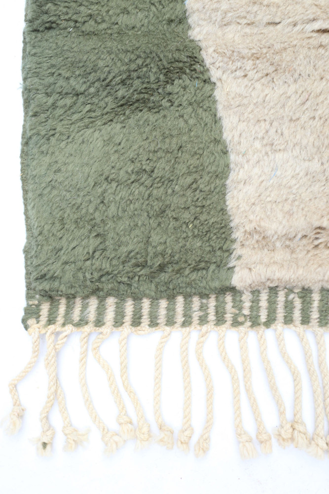 Tapis berbère aux teintes vertes et beiges, avec des motifs géométriques et des franges tressées.