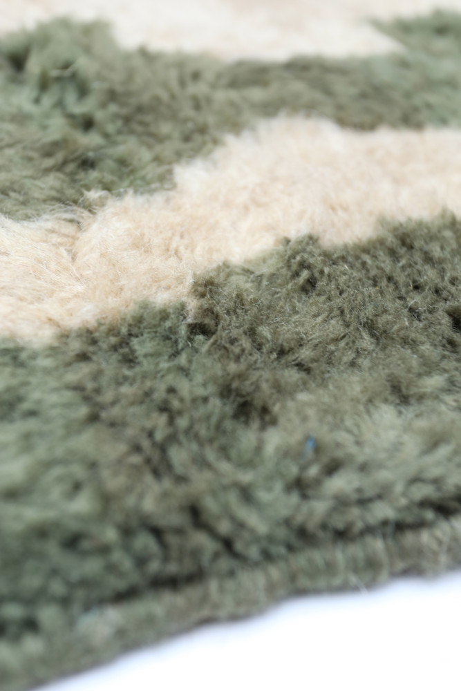 Tapis berbère aux motifs abstraits, couleurs vert olive et beige, offrant une texture douce et chaleureuse.
